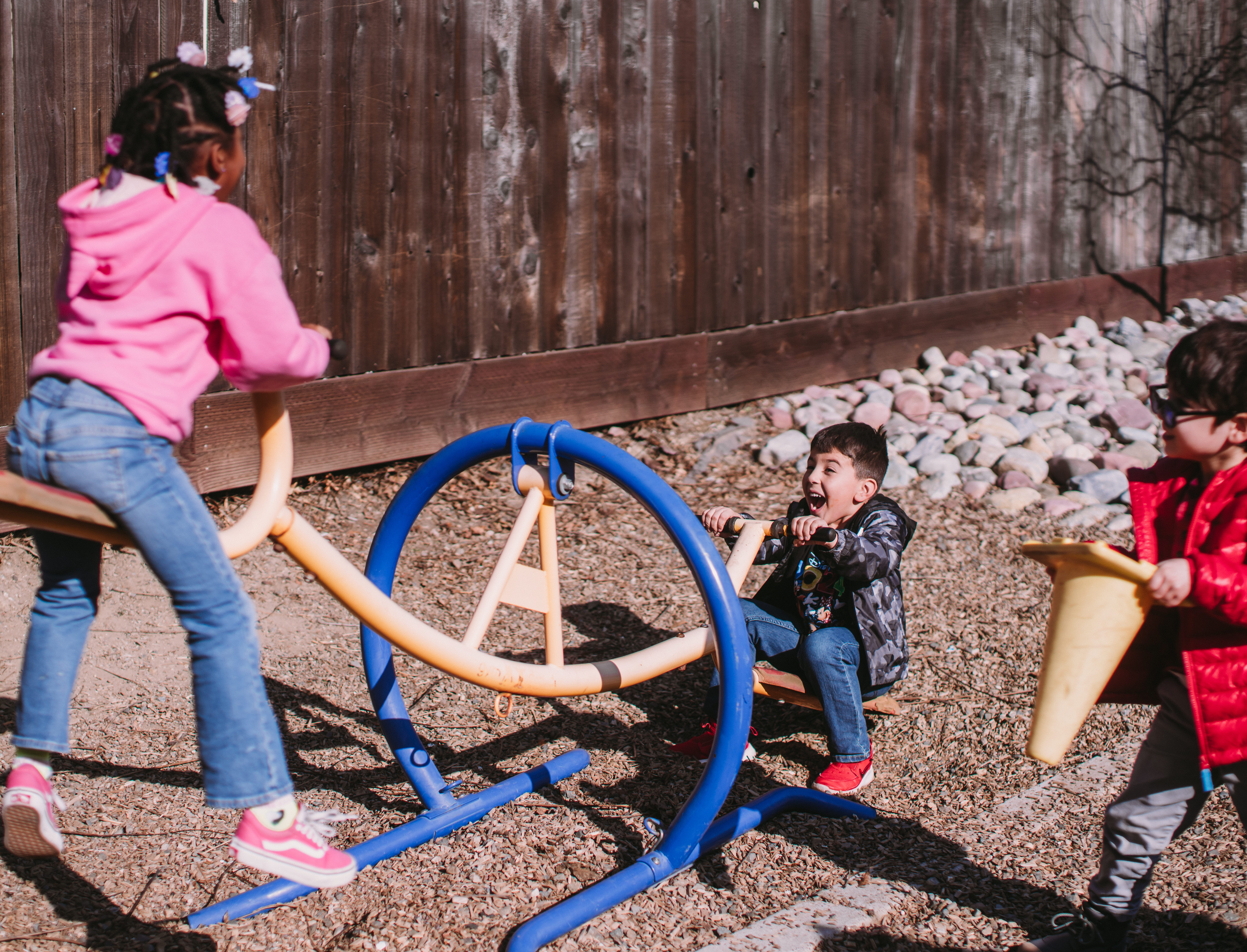 A boy and a girl playing on a seesaw in the school's kindergarden playground.